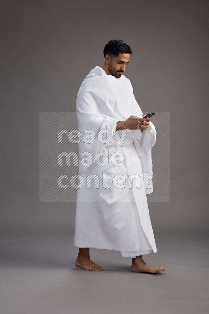 A man wearing Ehram Standing texting on phone on gray background