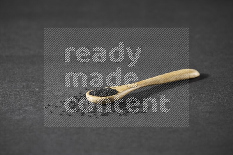 A wooden spoon full of black seeds and seeds spread beside it on a black flooring