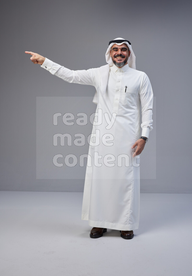Saudi man Wearing Thob and white Shomag standing interacting with the camera on Gray background