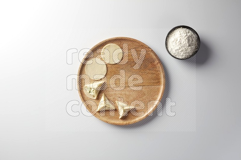 two closed sambosas and one open sambosa filled with cheese while flour aside in a wooden dish on a white background