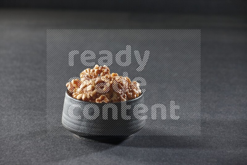 A black pottery bowl full of peeled walnuts on a black background in different angles
