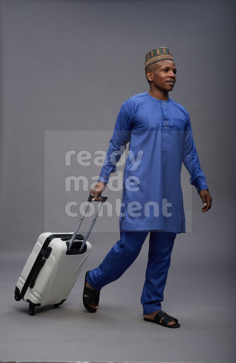 Man wearing Nigerian outfit standing holding bag on gray background