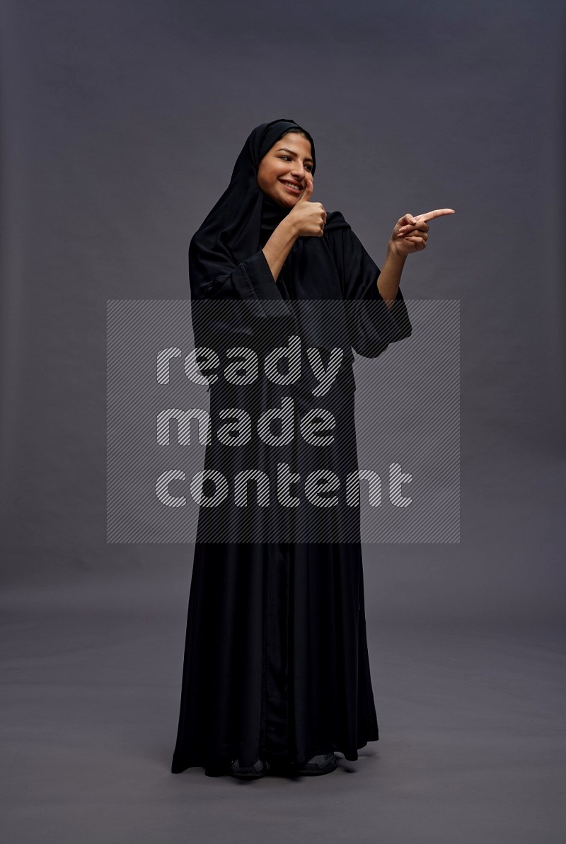 Saudi woman wearing Abaya standing interacting with the camera on gray background