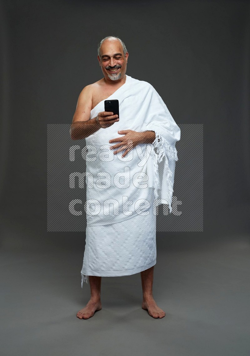 A man wearing Ehram Standing texting on phone on gray background