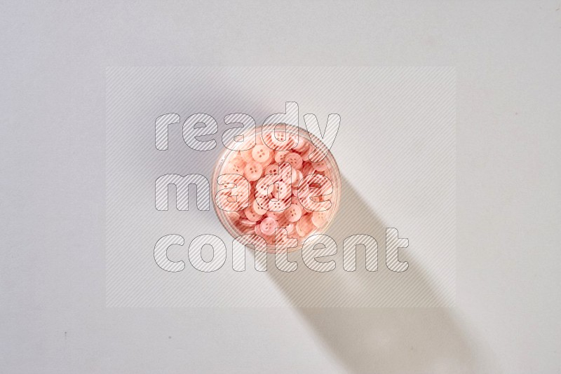 A glass jar full of colored buttons on grey background