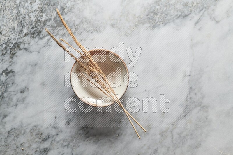 Wheat stalks on multicolored pottery plate on grey marble background