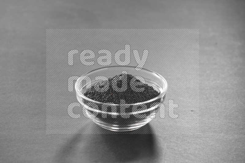 A glass bowl full of black seeds on black flooring