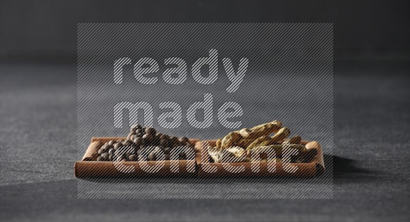 مربعان من أعواد القرفة ممتلئان ببهار الفلفل الحلو وأصابع الكركم علي خلفية سوداء