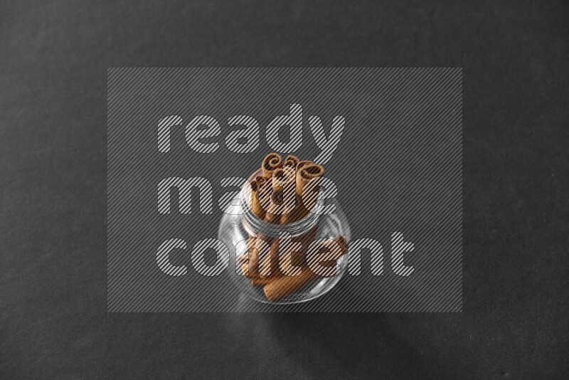 A glass spice jar full of cinnamon sticks on black flooring