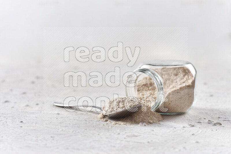 A glass jar full of onion powder flipped with some spilling powder on white background