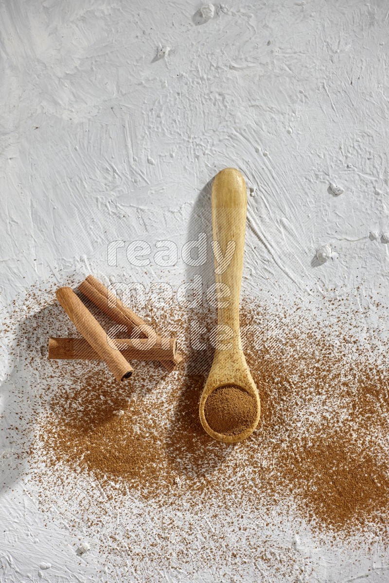 Cinnamon powder in a wooden spoon with cinnamon sticks and sprinkles powder on the flooring on white background