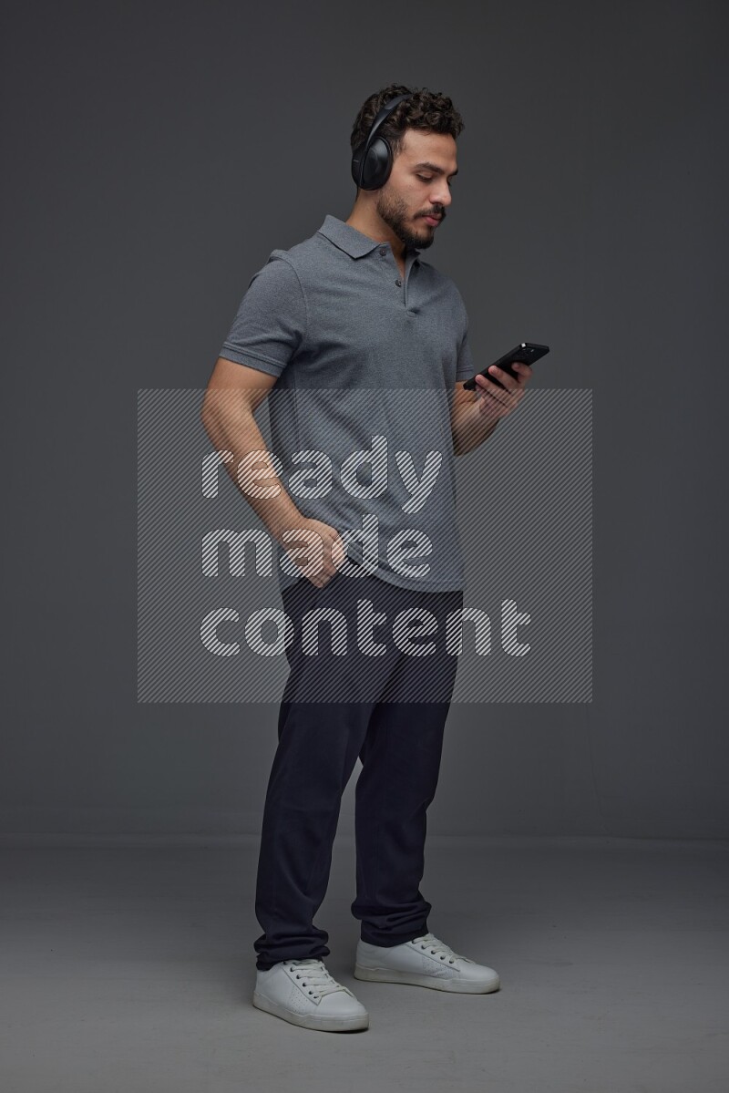 A man wearing casual and using his phone and headphone eye level on a gray background