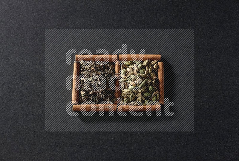 2 squares of cinnamon sticks full of cardamom and dried basil on black flooring