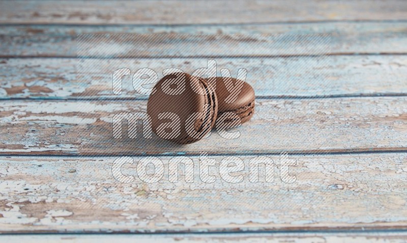 45º Shot of two Brown Dark Chocolate macarons on light blue wooden background