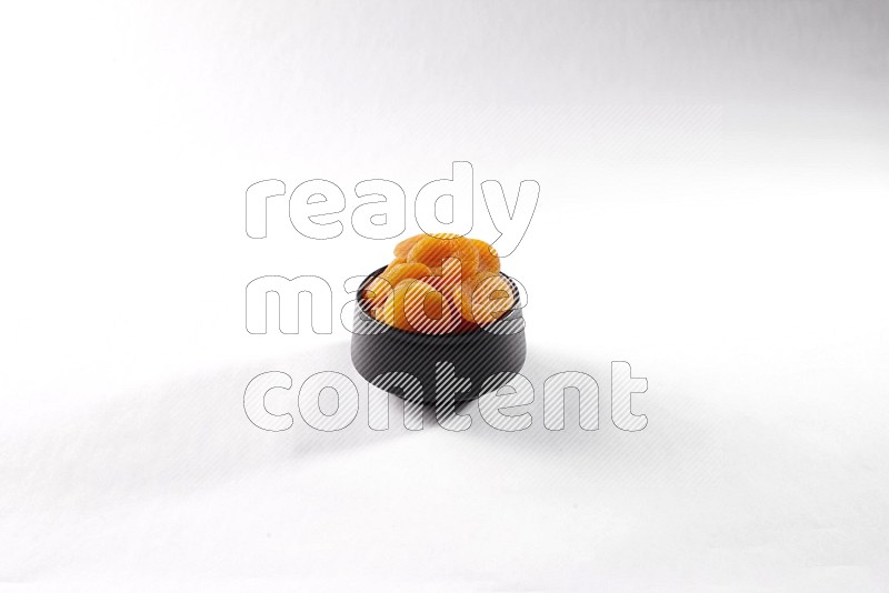 Dried apricots in a black pottery bowl on white background