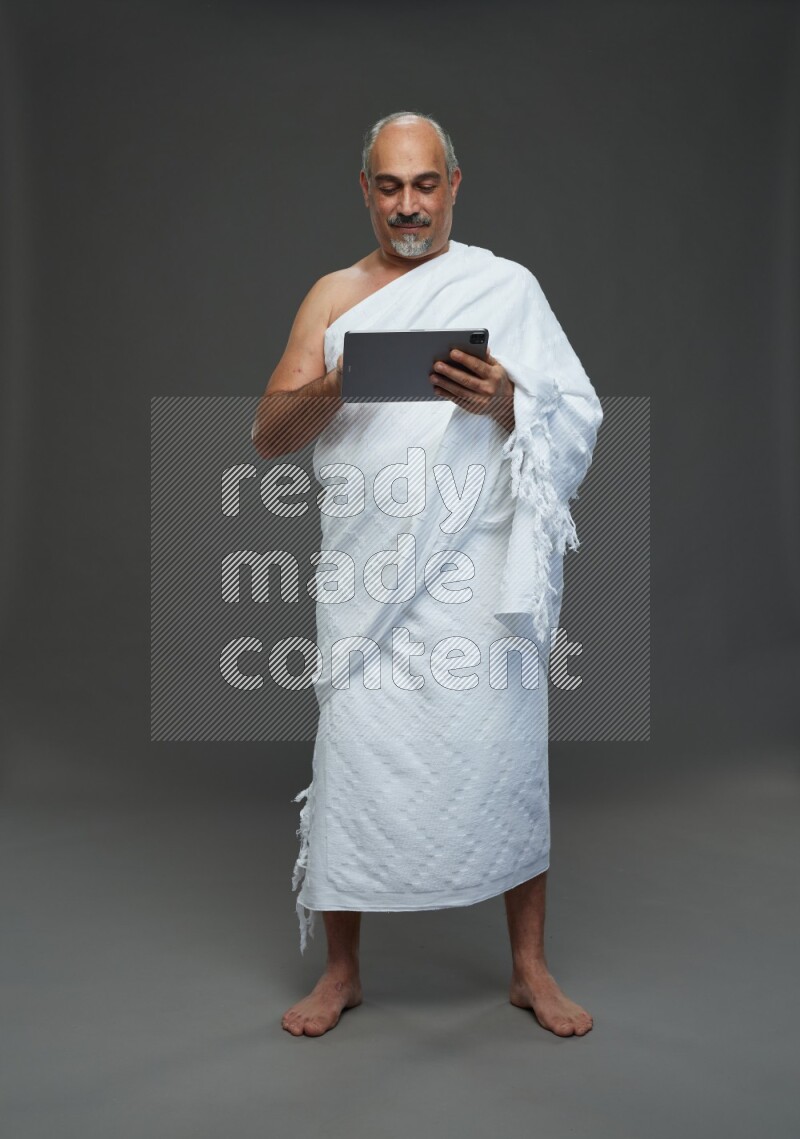 A man wearing Ehram Standing working on tablet on gray background