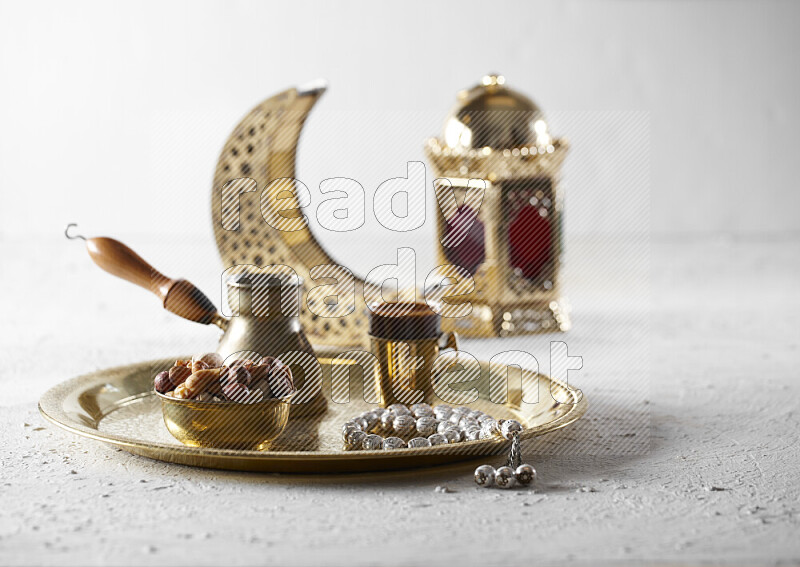 Nuts in a metal bowl with coffee and prayer beads on a tray beside lanterns in a light setup