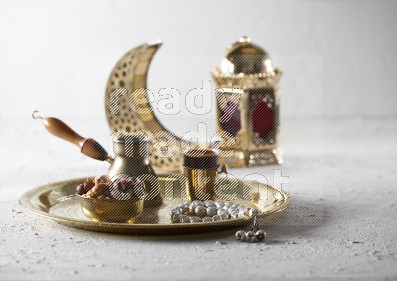 Nuts in a metal bowl with coffee and prayer beads on a tray beside lanterns in a light setup
