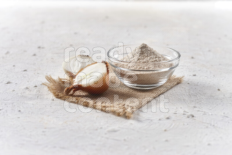 A glass bowl full of onion powder on burlap fabric on white background