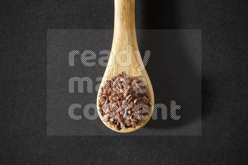 A wooden spoon full of flaxseeds on a black flooring