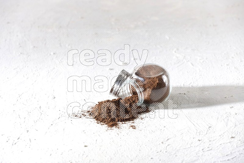 A flipped glass spice jar full of cloves powder and powder came out of it on textured white flooring