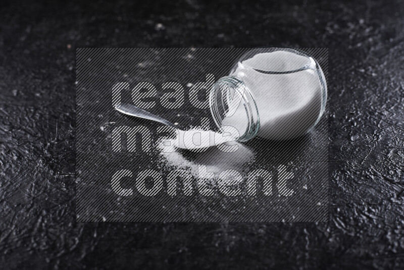 A glass jar full of fine table salt on black background