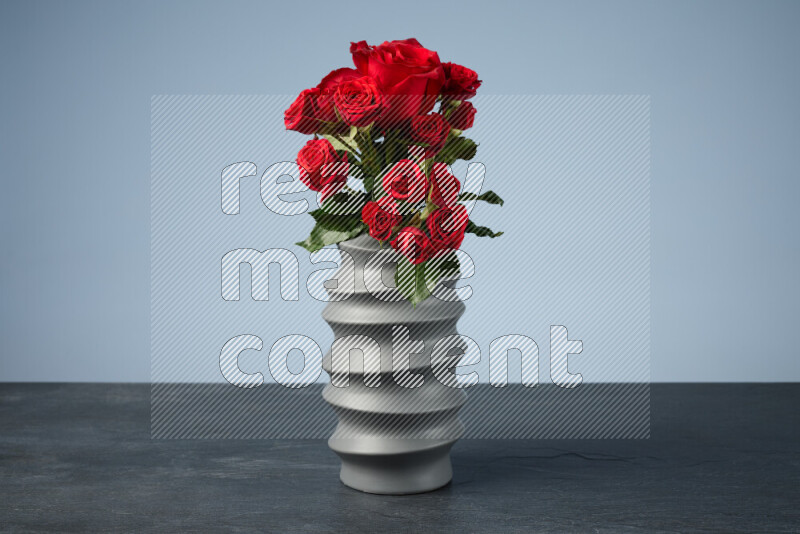 An arrangement of vivid red roses in a grey spiral vase on black marble background