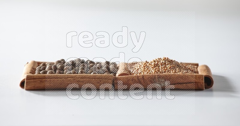 مربعان من أعواد القرفة ممتلئان بحبوب الخردل وحبوب بهار الفلفل الحلو علي خلفية بيضاء