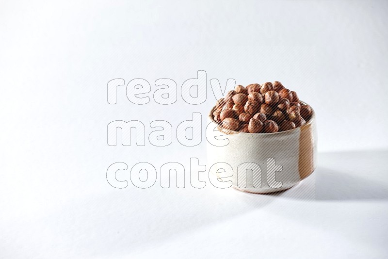 A beige ceramic bowl full of peeled hazelnuts on a white background in different angles