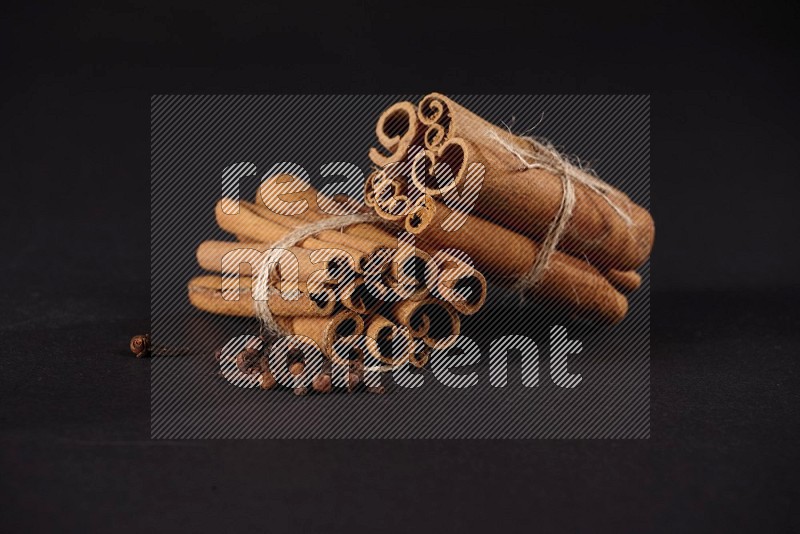 Two bounded stacks of cinnamon sticks with cloves on black background