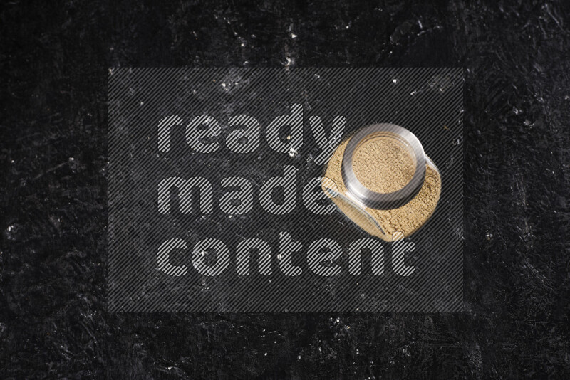 A glass jar full of ground ginger powder on black background