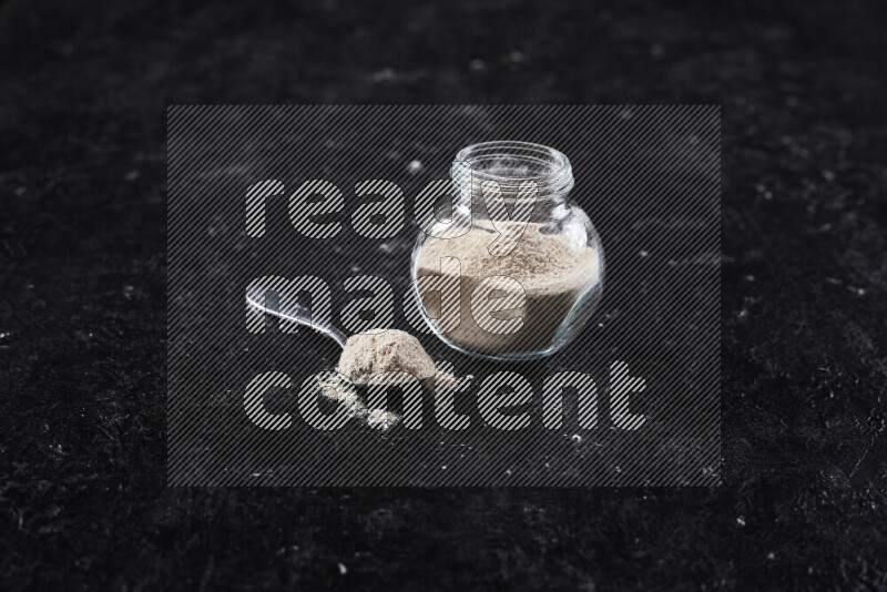 A glass jar full of onion powder on black background