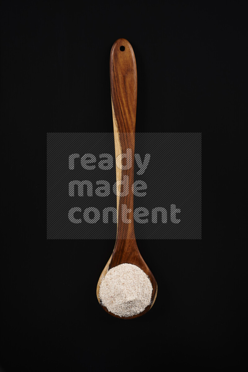 A wooden ladle full of onion powder on black background