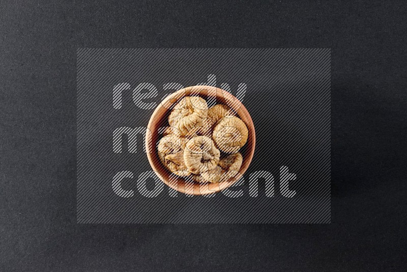 A wooden bowl full of dried figs on a black background in different angles