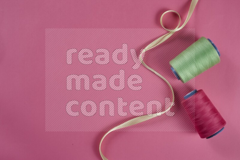 A green and pink collection of sewing and tailoring tools arranged on a pink background