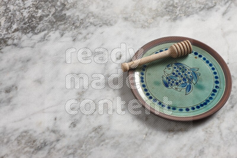 Decorative pottery plate with wooden honey dipper in it on grey marble background
