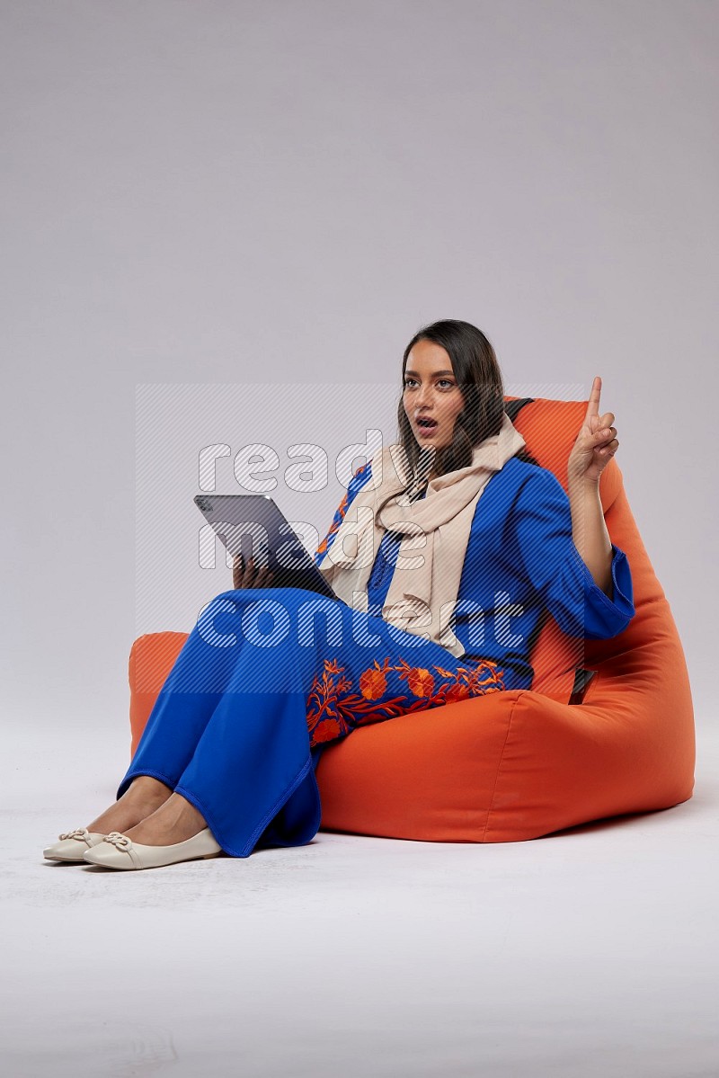 A Saudi woman sitting on an orange beanbag and working on tablet