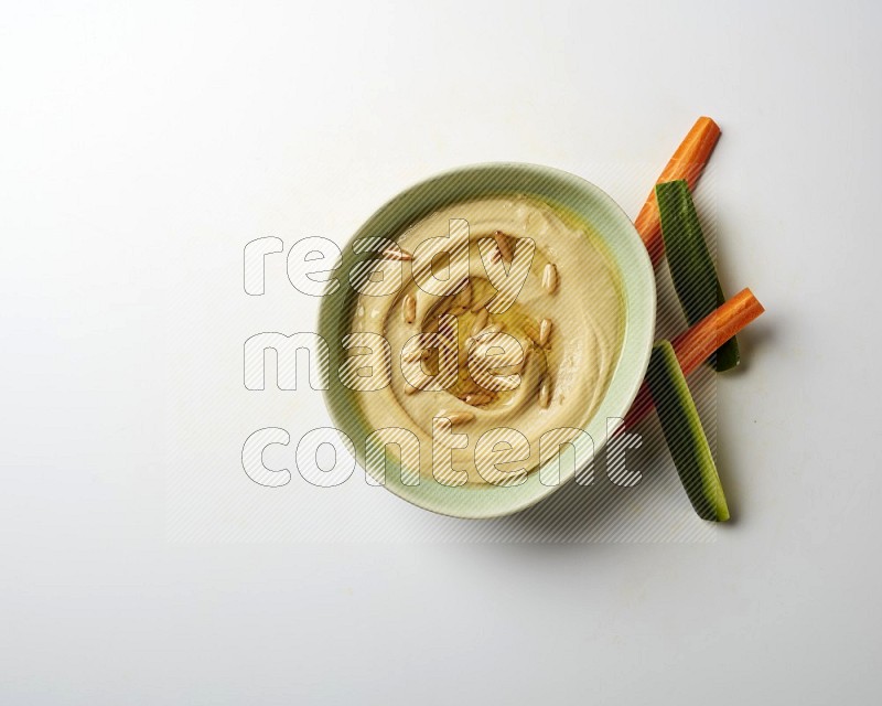 Hummus in a green plate garnished with pine nuts on a white background