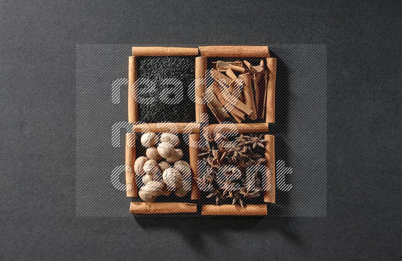 4 squares of cinnamon sticks full of black seeds, cinnamon, star anise and nutmegs on black flooring