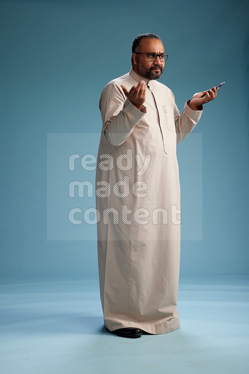 Saudi Man without shimag Standing texting on phone on blue background