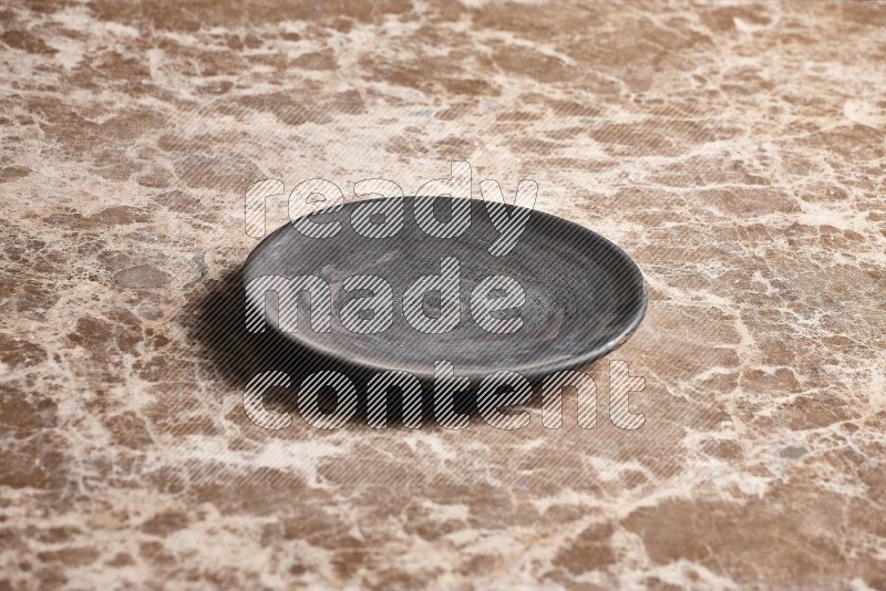 A circular black pottery plate on beige marble background