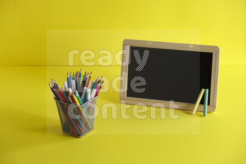 A blackboard with different school supplies on yellow background