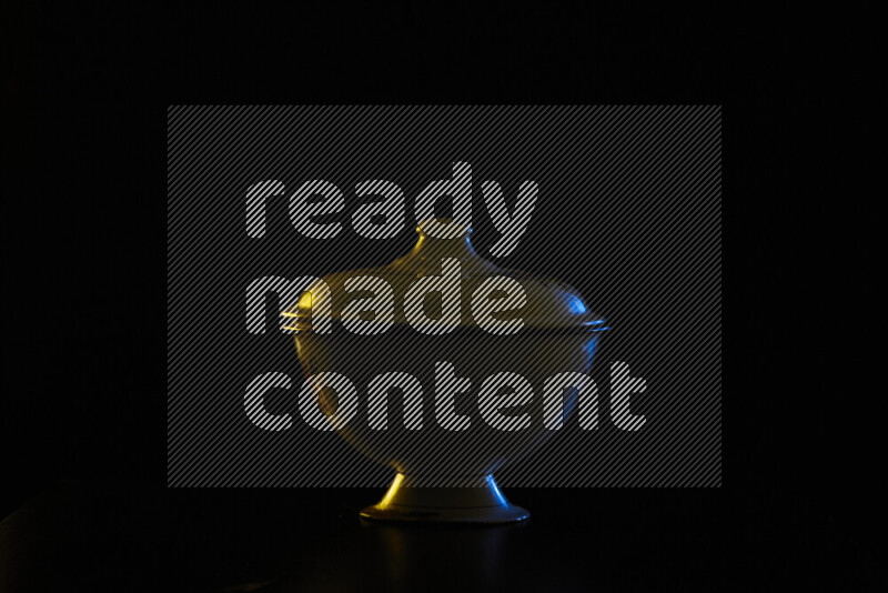 A vintage metal pot with colored rim light against black background