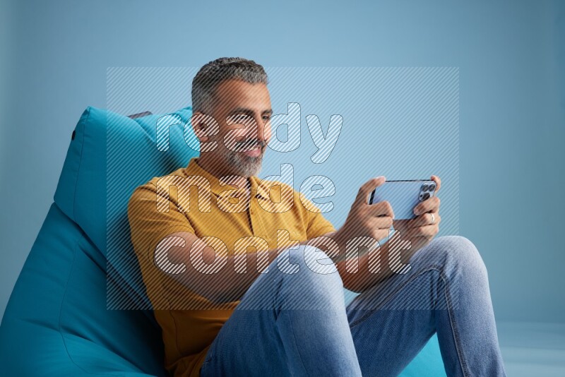 A man sitting on a blue beanbag and playing on phone