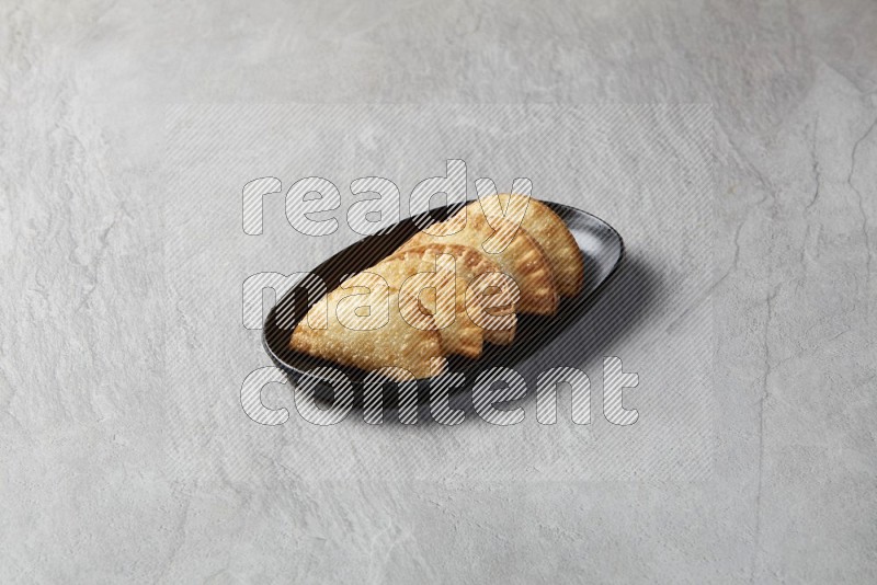 Five fried sambosas in an oval shaped black plate on a gray background