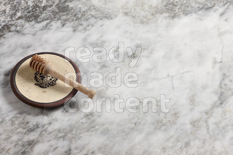 Decorative Pottery Plate with wooden honey handle in it, on grey marble flooring, 65 degree angle