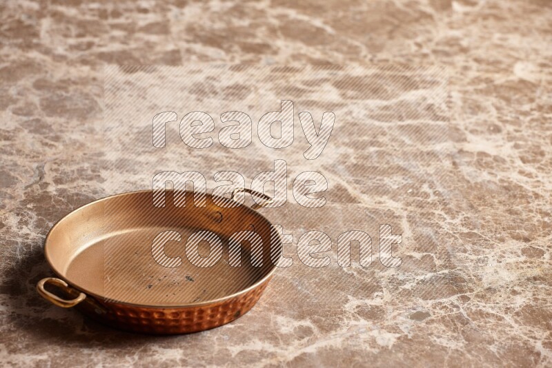 A small copper pan on beige marble background