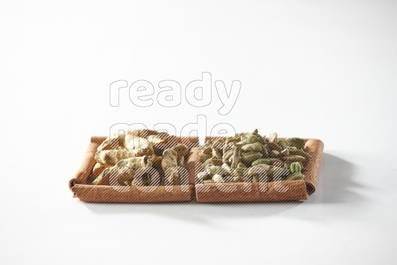 مربعان من أعواد القرفة ممتلئان بحبوب الهيل وأصابع الكركم علي خلفية بيضاء