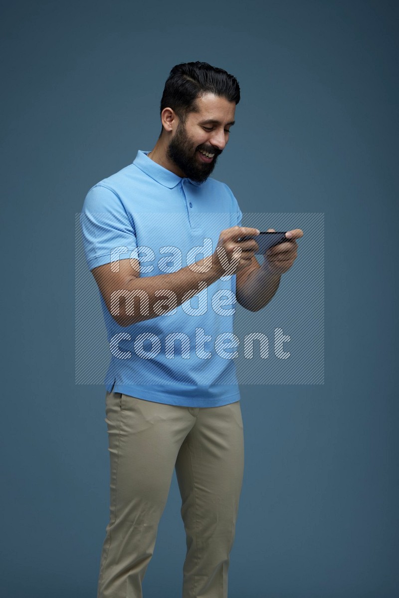Man playing a game on his phone in a blue background wearing a Blue shirt