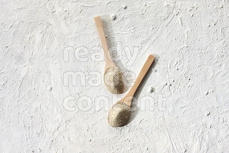 2 wooden spoons full of white pepper powder on textured white flooring